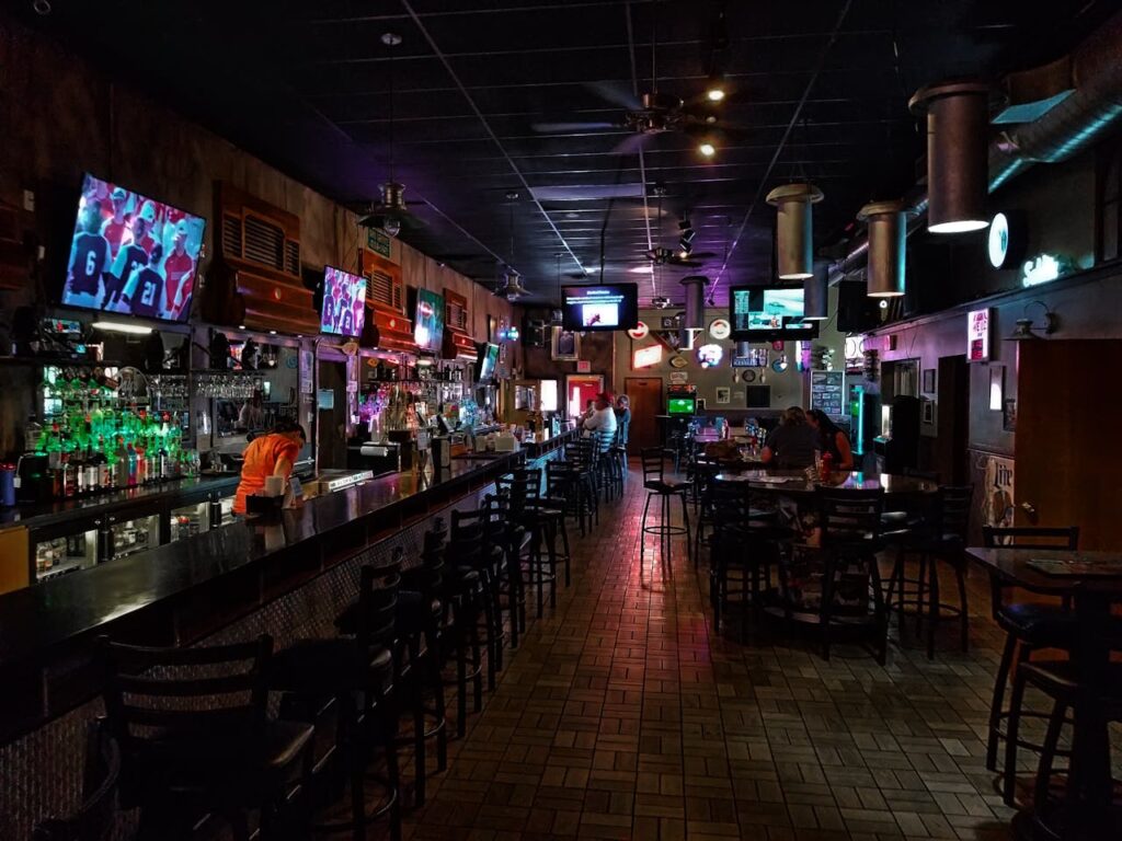 pexels-photo-2585614 A dimly lit modern bar interior featuring a long counter and multiple screens, creating a cozy urban atmosphere.